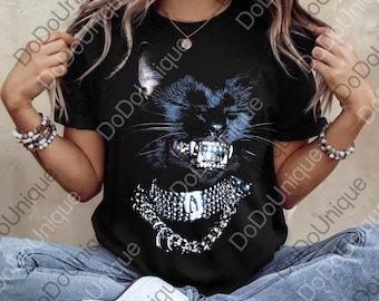 Op de afbeelding: Zwart T-shirt met een afbeelding van een zwarte kat met een woeste uitdrukking en een zilveren ketting. De tanden van de kat zijn ook zilver. Het shirt heeft korte mouwen en wordt door een persoon gedragen.