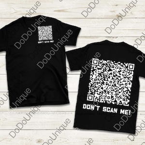 Può includere: Due magliette nere con codici QR bianchi e la scritta "DON'T SCAN ME!". Una maglietta ha un piccolo codice QR sul davanti, l'altra un grande codice QR sul retro. Presentate su una superficie a venature di legno chiaro.