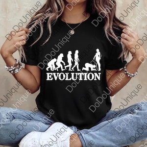 May include: Black t-shirt featuring a white graphic of the evolution of humans, with the word "EVOLUTION" below. The design depicts a progression from ape-like figures to a person kneeling. The shirt is a classic crew neck.