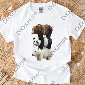 May include: White t-shirt featuring a graphic of three bears stacked on top of each other: a brown bear, a panda bear, and a polar bear. The shirt has a crew neck and short sleeves. The brand name "GILDAN" is visible on the tag.