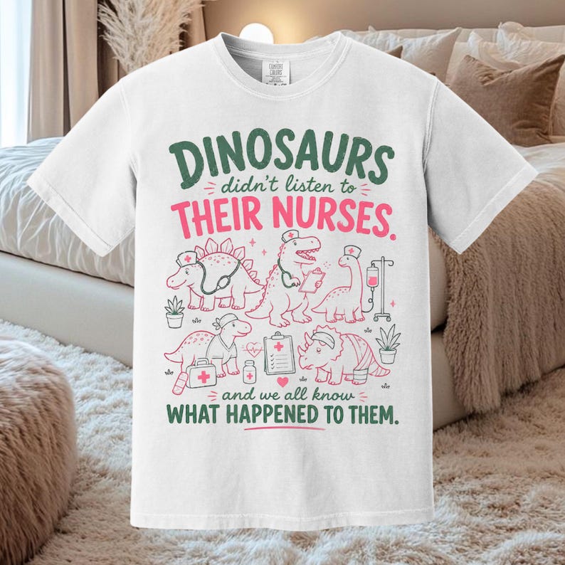 Op de afbeelding: Een wit T-shirt met korte mouwen en een afbeelding van vijf dinosaurussen verkleed als verpleegkundigen met medische hulpmiddelen. De tekst luidt: DINOSAURS didn't listen to THEIR NURSES. and we all know WHAT HAPPENED TO THEM. Groene en roze opdruk.