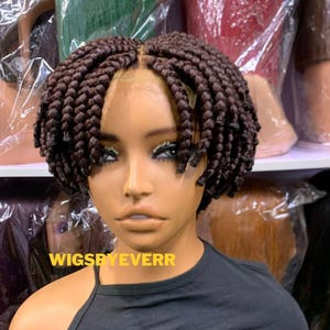May include: A dark brown braided wig with a short, chin-length bob cut on a mannequin head. The wig features a centre part and uniform, thick box braids. The text WIGSBYEVERR is printed in yellow across the lower portion of the image.