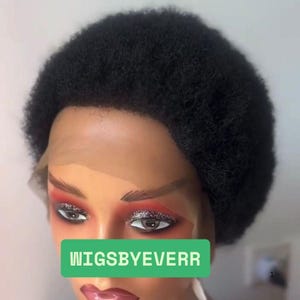 Könnte beinhalten: Schwarze Afro-Perücke auf einem Schaufensterkopf. Die Perücke hat ein natürliches, strukturiertes Aussehen. Die Schaufensterpuppe hat Make-up mit rotem und silbernem Lidschatten und ein grünes Rechteck mit dem Text "WIGSBYEVERR".