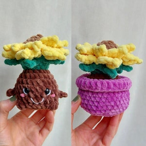 Puede incluir: Dos peluches de girasol tejidos a crochet. Un girasol es marrón y tiene una cara feliz. El otro girasol está en una maceta morada.