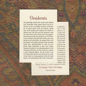 May include: Two white cards with the text "Desiderata" and other text in a serif font. The cards are on a patterned fabric background. The text includes inspirational quotes and the author's name, Max Ehrmann.