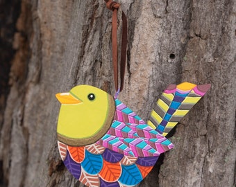 May include: A colorful wooden bird ornament with a yellow head, purple, pink, orange, and blue wings, and a brown string for hanging.