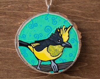 May include: Hand-painted wooden ornament featuring a yellow and black bird perched on a branch. The bird is set against a teal background with blue swirls, within a circular wood slice. A twine loop is attached for hanging.