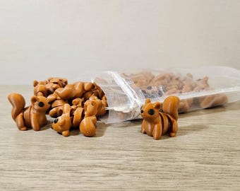 May include: A collection of small, brown squirrel figurines, some standing and others spilling from a clear plastic bag. The squirrels have detailed features, including striped tails and dark eyes. The figurines are on a wooden surface.