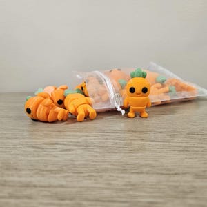 May include: A collection of orange carrot-shaped erasers, some lying on a wooden surface and others inside a clear bag. One eraser is a standing cartoon carrot figure with a green top. The erasers are a bright orange color.