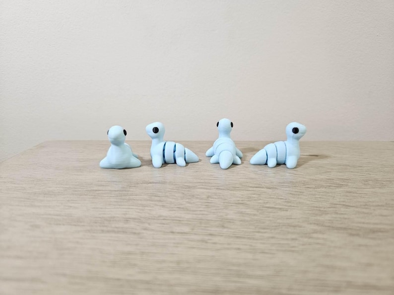 May include: Four small, light blue clay sculptures of a sea creature, each with black eyes. Two are in a seated position, and two are in a crawling position. The sculptures are on a light brown wooden surface.