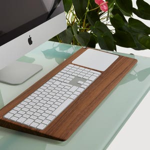 Puede incluir: Un conjunto de teclado y trackpad de madera con un teclado y trackpad blancos sobre una superficie verde claro.
