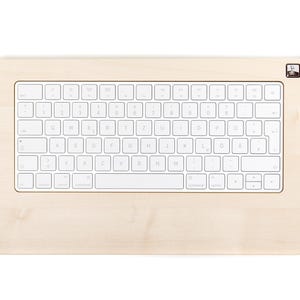 Könnte beinhalten: Ein hellfarbiger Holz-Tastaturrahmen mit einer weißen Tastatur. Die Tastatur hat weiße Tasten mit schwarzer Beschriftung. Der Rahmen hat eine glatte, natürliche Holzmaserung und ein kleines Logo in der oberen rechten Ecke.