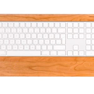 Könnte beinhalten: Eine weiße drahtlose Tastatur mit einem Holzrahmen. Die Tastatur verfügt über einen Nummernblock und Funktionstasten.