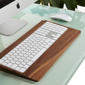 Puede incluir: Un teclado inalámbrico blanco con un soporte de madera de nogal. El teclado está sobre una superficie de vidrio verde claro.