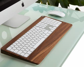 Puede incluir: Un teclado inalámbrico blanco con un soporte de madera de nogal. El teclado está sobre una superficie de vidrio verde claro.