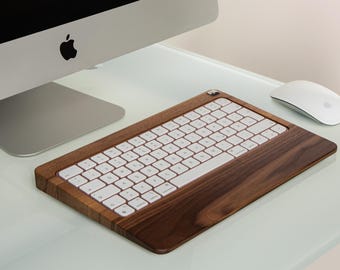 Puede incluir: Un teclado inalámbrico blanco con una base de madera de nogal. El teclado está inclinado hacia arriba y tiene un ratón blanco a su lado.