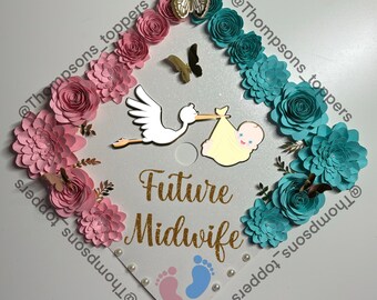 Pode incluir: Um chapéu de formatura decorado com flores de papel rosa e azul, uma cegonha carregando um bebê e o texto "Future Midwife".