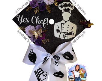 Pode incluir: Um chapéu de formatura preto decorado com flores de papel roxas e douradas, uma borboleta dourada e uma silhueta de chef. O texto "Yes Chef!" é exibido. Uma fita branca com ícones relacionados a alimentos está anexada.