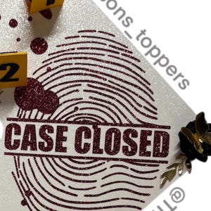 Puede incluir: Una superficie blanca brillante con un dise&ntilde;o de huella dactilar grande en purpurina burdeos. Las palabras "CASE CLOSED" est&aacute;n sobre la huella dactilar. Tambi&eacute;n hay marcadores de evidencia amarillos con n&uacute;meros negros y una cinta amarilla de la escena del crimen.