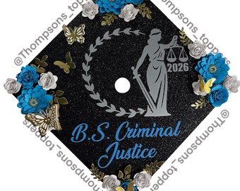 Pode incluir: Um chapéu de formatura preto decorado com flores de papel azuis, borboletas prateadas e douradas e rosas prateadas. O texto "B.S. Criminal Justice" é azul, e uma figura prateada da Dama da Justiça está no centro.