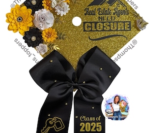 Pode incluir: Um chapéu de formatura dourado com glitter, adornado com flores de papel pretas, brancas e amarelas e uma borboleta dourada. O chapéu apresenta o texto "Real Estate Agents NEED CLOSURE" e um laço preto com "Class of 2025".