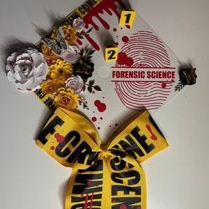 May include: A graduation cap decorated with paper flowers, a butterfly, and a yellow ribbon with "CRIME SCENE" text. The cap features a fingerprint design, blood spatter, and the words "FORENSIC SCIENCE".