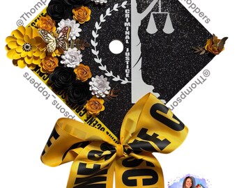 Pode incluir: Um chapéu de formatura preto decorado com flores de papel amarelas e pretas, borboletas e uma fita que diz "CRIME SCENE". O chapéu apresenta uma silhueta da Dama da Justiça e as palavras "CRIMINAL JUSTICE".