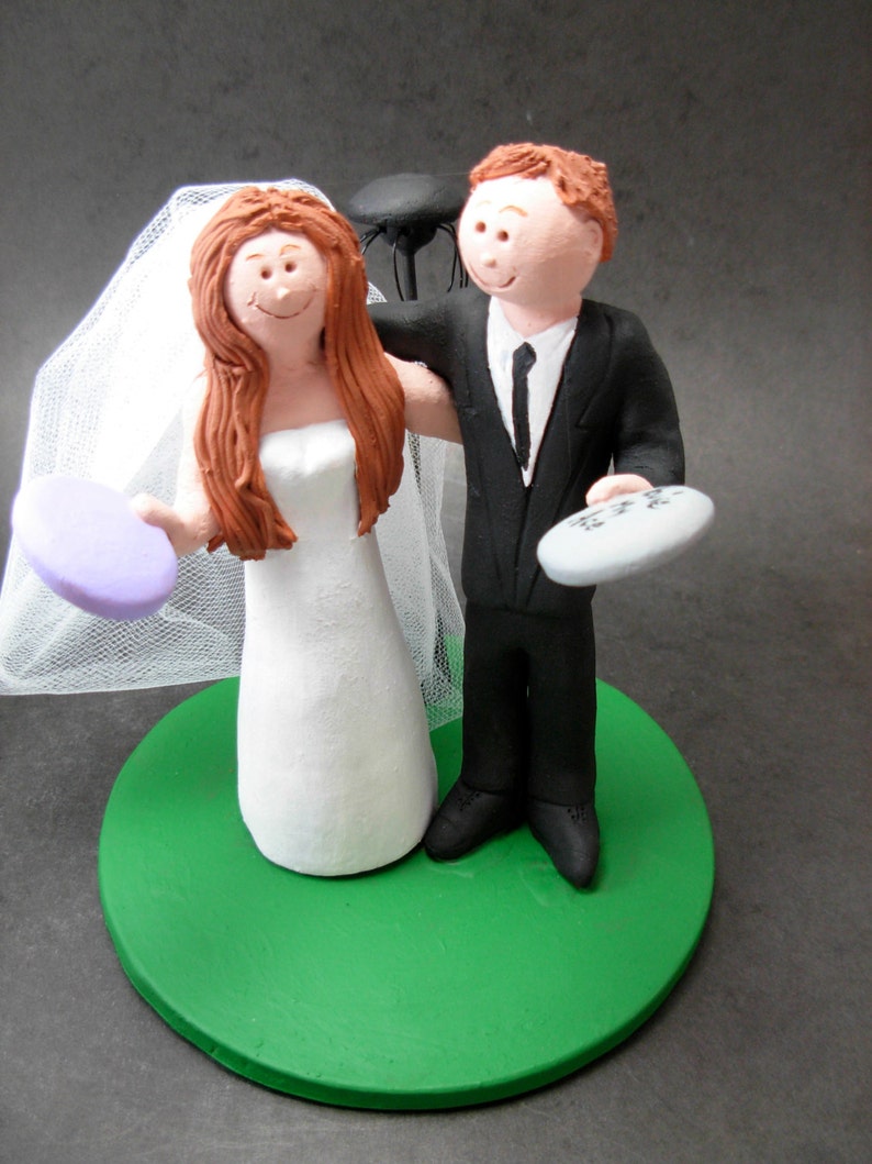 May include: A wedding cake topper featuring a bride and groom figurine. The bride is wearing a white dress and a veil. The groom is wearing a black suit and a tie. The cake topper is on a green base.