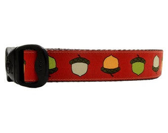 May include: A red dog collar with a repeating pattern of acorns in shades of green, brown, and orange. The collar has a black plastic buckle.