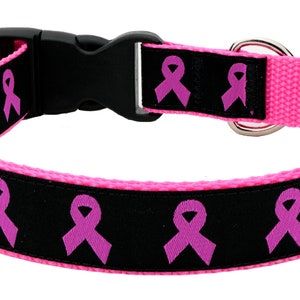 Op de afbeelding: Roze en zwarte hondenriem met een roze lintpatroon. De riem heeft een plastic gesp en een metalen D-ring.