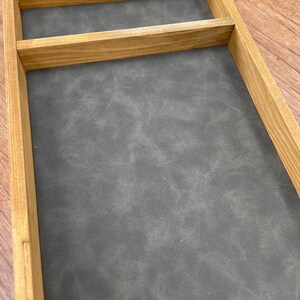 May include: A wooden tray with a gray felt lining and a single divider. The tray is made of natural wood with a light brown finish.