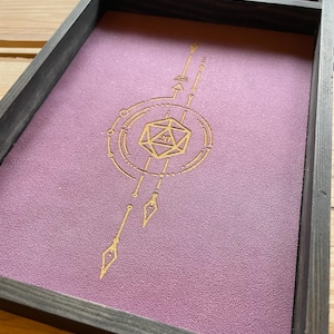 May include: A wooden dice tray with a purple felt lining and a gold geometric design featuring a 20-sided die in the center.