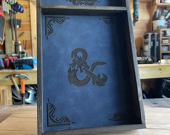 May include: A wooden dice tray with a blue felt lining and a black leatherette inlay featuring the Dungeons & Dragons logo and a stylized dragon and ampersand.