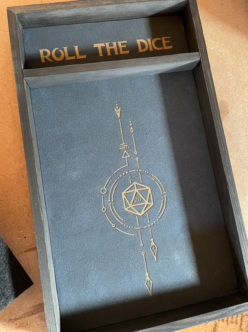 May include: A wooden dice tray with a black felt lining and a gold design featuring a 20-sided die and the text "ROLL THE DICE".