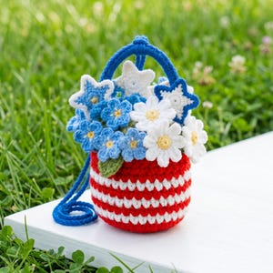 May include: A crocheted basket with red and white horizontal stripes, featuring a blue handle and a decorative arrangement of blue and white crocheted flowers and stars. The basket is crafted with yarn and includes a small green leaf accent.
