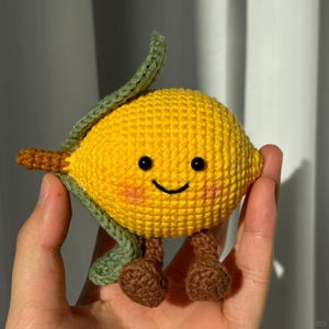 May include: A crocheted lemon toy with a cheerful face, green leaf, and brown stem and legs. The yellow body is detailed with crochet stitches. A charming, handmade soft toy.