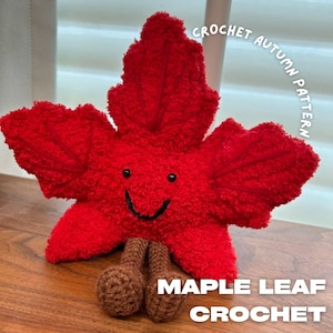 Puede incluir: Una creación de ganchillo con forma de hoja de arce roja, con una cara sonriente y patas marrones en forma de tallo. Se ve el texto "CROCHET AUTUMN PATTERN" y "MAPLE LEAF CROCHET".