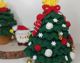 May include: Crocheted Christmas tree with a yellow star, red bow, and candy cane. The green tree is decorated with white and red ornaments, gold bells, and white snowflakes. The tree sits on a brown crocheted base.