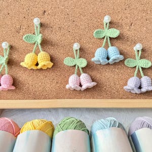 May include: Crocheted tulip decorations in pink, yellow, blue, and lavender, attached to a corkboard with push pins. The tulips have green stems and leaves. Below are rolls of yarn in matching colors.