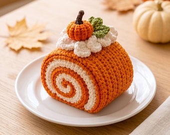 May include: A crocheted pumpkin roll cake featuring orange and white yarn swirls, topped with white crocheted frosting, a small orange pumpkin, and two green leaves. The item is displayed on a white plate, showcasing detailed yarn texture.