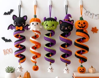 May include: Five hanging crochet decorations featuring a bat, a ghost, a green monster, a black cat in a purple hat, and a jack-o'-lantern. Each figure is attached to a colorful spiral tail in orange, black, and purple, accented with small beads.