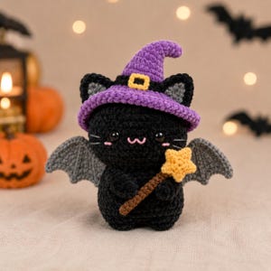 May include: A black crocheted cat plush toy wearing a purple witch hat with a yellow buckle. The cat has gray bat wings, black plastic eyes, pink stitched cheeks, and a pink mouth. It holds a brown wand topped with a yellow crocheted star.