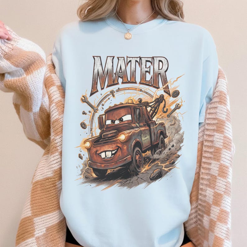 Pu&ograve; includere: Felpa azzurra con un'immagine a cartoni animati di Cricchetto del film Cars. La grafica mostra Cricchetto con un volto sorridente, circondato da attrezzi e fulmini, con la scritta "MATER" sopra.
