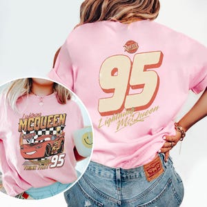 Op de afbeelding: Zachtroze T-shirt met Lightning McQueen uit de film Cars. De voorkant toont het personage en het nummer 95. De achterkant heeft een groot nummer 95 en de tekst "Lightning McQueen".