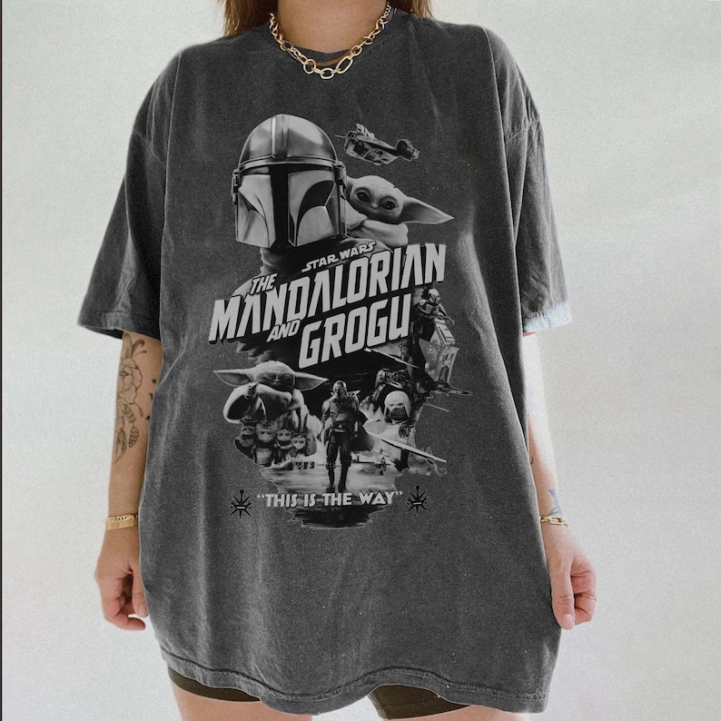 以下が含まれることがあります： スターウォーズシリーズ「マンダロリアンとグローグ」のグラフィックが特徴の濃いグレーのTシャツ。デザインにはマンダロリアンのヘルメット、グローグ、「This is the Way」というフレーズが含まれています。シャツはヴィンテージ感があります。