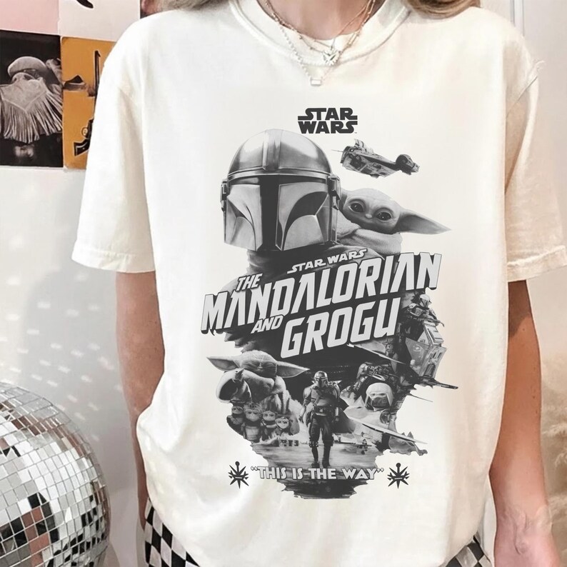 以下が含まれることがあります： スターウォーズシリーズの白黒グラフィックが特徴のクリーム色のTシャツ。「STAR WARS」、「THE MANDALORIAN AND GROGU」、「THIS IS THE WAY」の文字と、キャラクターや宇宙船の画像が含まれています。