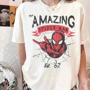 May include: A white ceramic mug with a black handle and the text "But First, Coffee" in a bold, black font. The mug is set against a blurred background, suggesting a cosy setting.