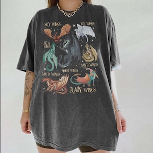 May include: Dark gray t-shirt featuring a fantasy dragon graphic. The design includes various dragon types labeled "Sky Wings," "Ice Wings," "Sea Wings," "Mud Wings," "Night Wings," "Sand Wings," and "Rain Wings."