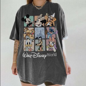 May include: Dark gray t-shirt featuring a colorful grid of Disney characters including Mickey Mouse, Minnie Mouse, and Goofy. The shirt has the text "Walt Disney World" in a script font.