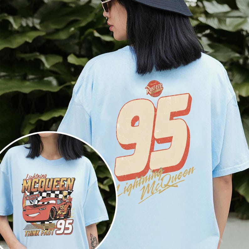 Op de afbeelding: Lichtblauw T-shirt met Lightning McQueen uit de film Cars. De voorkant toont de auto met de tekst "Lightning McQueen", "Think Fast" en "95". De achterkant heeft een grote "95" met "Lightning McQueen" en "Rusteze".